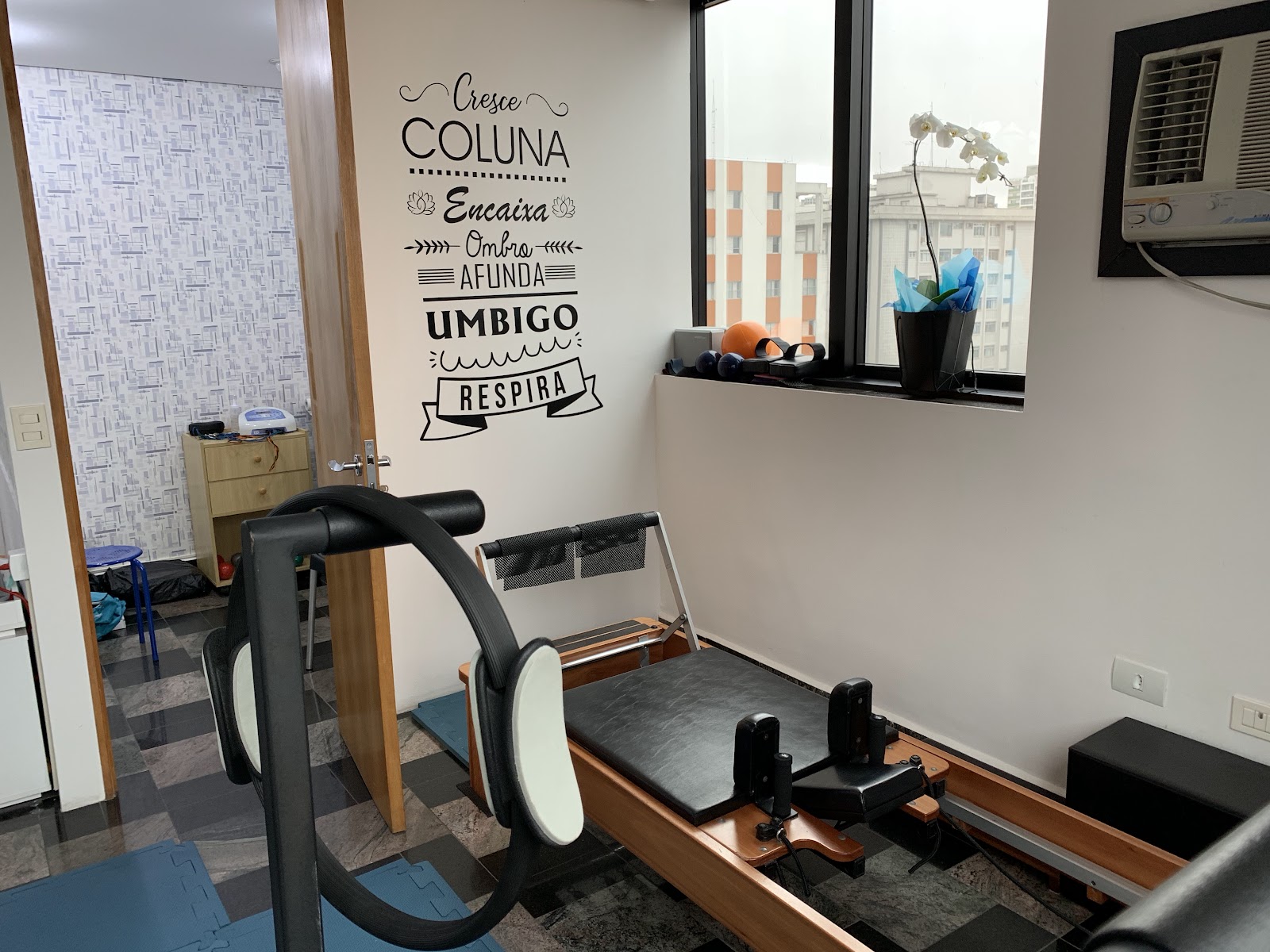 Reformer do estúdio diante da parede com o lettering: cresce coluna, encaixa ombro, afunda umbigo, respira