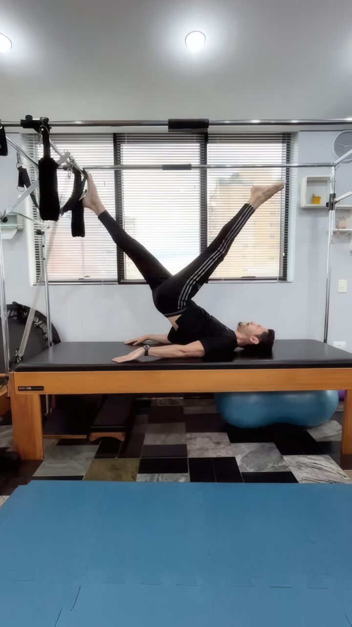 Aluna deitada no Cadillac elevando as pernas em um exercício de pilates
